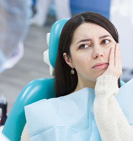 Woman in dental chair holding jaw